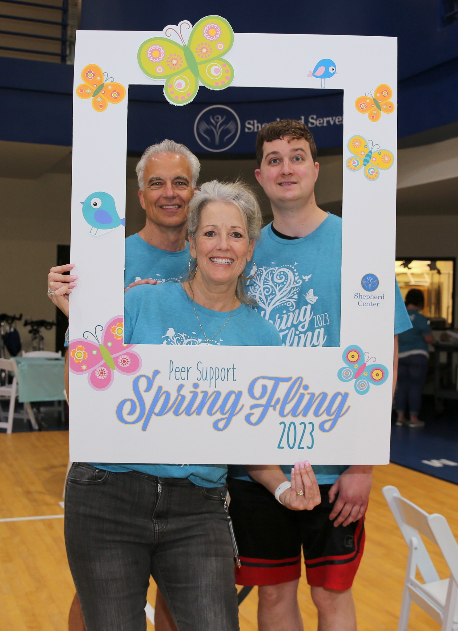 Peer Support Liaison, Mariellen Jacobs, poses behind a lifesize photo frame with two Shepherd patients. The frame reads, "Peer Support Spring Fling 2023."