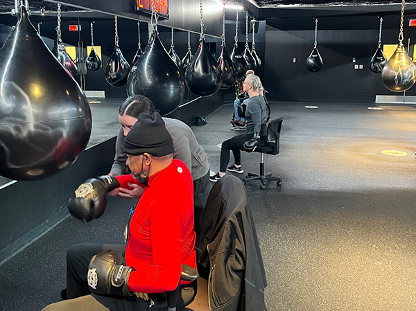 Gloved participants in the boxing clinic sit in chairs while hitting speedbags.