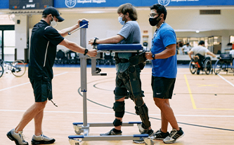 Male client uses the Rifton Pacer Gait Trainer to work on walking with his two exercise physiologists.