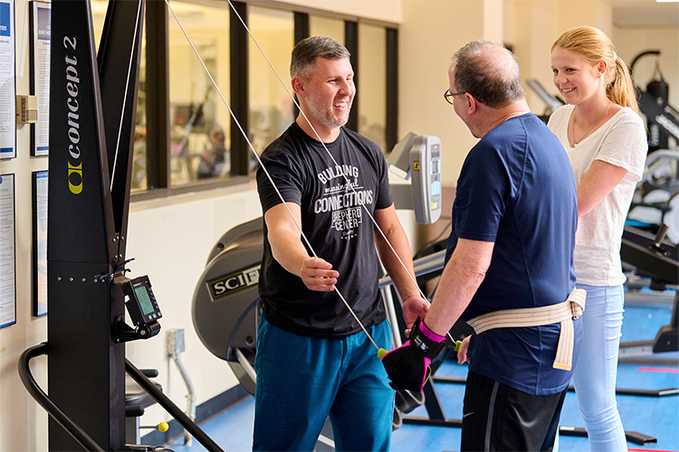 Richard utilizes a standing rowing machine as part of his arm strength recovery journey post-stroke. As he progressively regains function and strength in his left hand, he relies on a specialized grip aid to ensure a secure hold on the rowing bar.