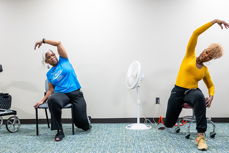 ProMotion member stretches to the side while participating in a chair fitness program, lead by an exercise physiologist