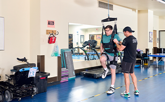 Male client using the ZeroG raises up his knee to practice walking with the help of his exercise physiologist.