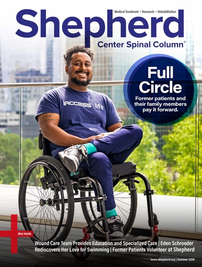 Brandon Winfield, founder of app iAccess Life, sits in his wheelchair on a balcony, smiling in front of cityscape background.