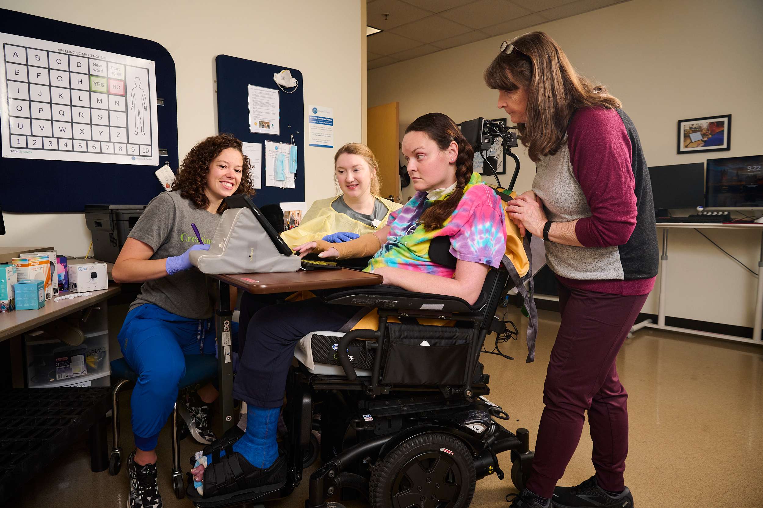 Female patient is learning to use hi-tech and mid-tech communication methods to communicate with assistive technology therapist and occupational therapist. Her mother also participates in the education and therapy.