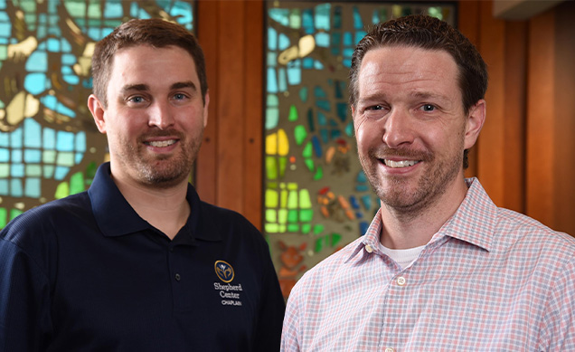 Chaplains Ben Rose and Dave Wethington smile in front of the stained glass windows in the chapel at Shepherd Center.