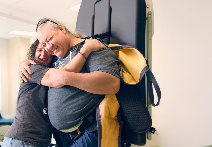 Physical therapist leans in to give a male patient a big hug during a therapy session.