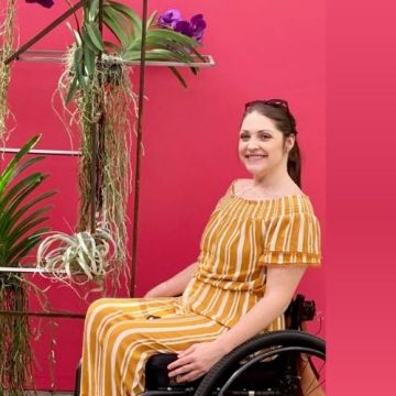 Megan Collins, an attendee of the spinal cord injury survivor peer support group, sits by a plant, smiling.