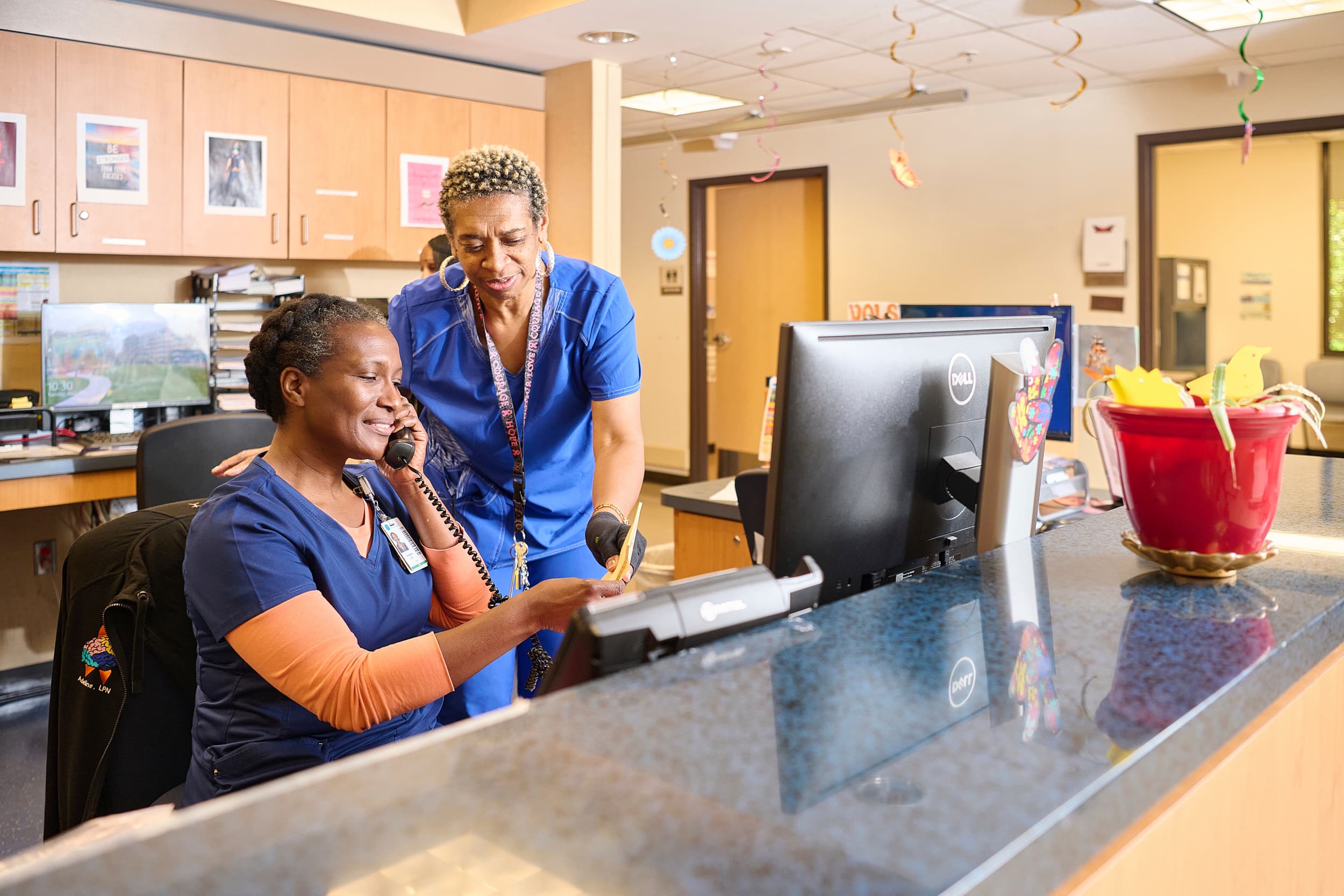 Two female medical assistants manage administrative duties behind a nursing station.