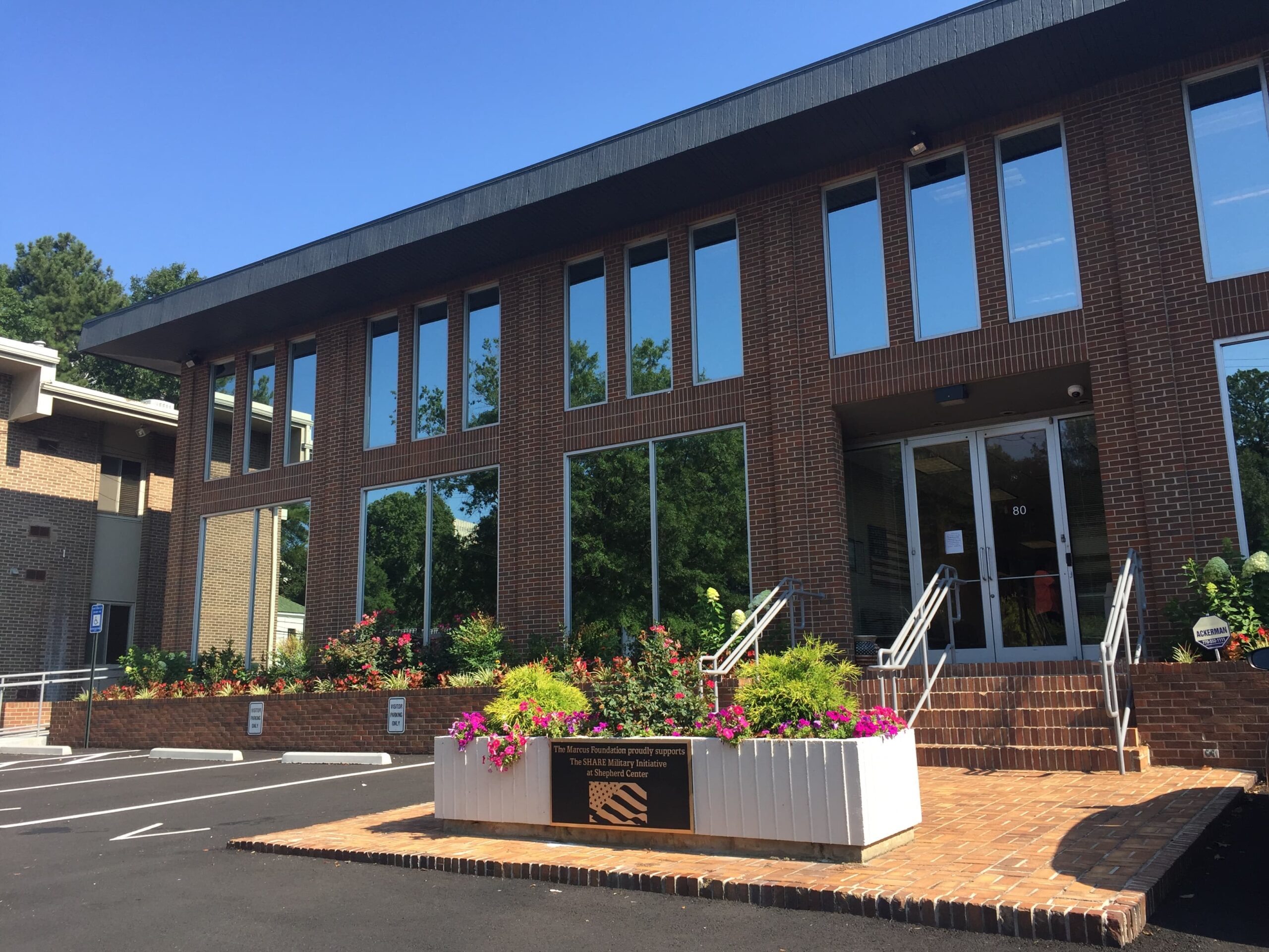 An outside view of the 80 Peachtree Park, a two story brick building with lots of windows and flowers out front, that houses the SHARE Military Initiative and Complex Concussion Clinic.