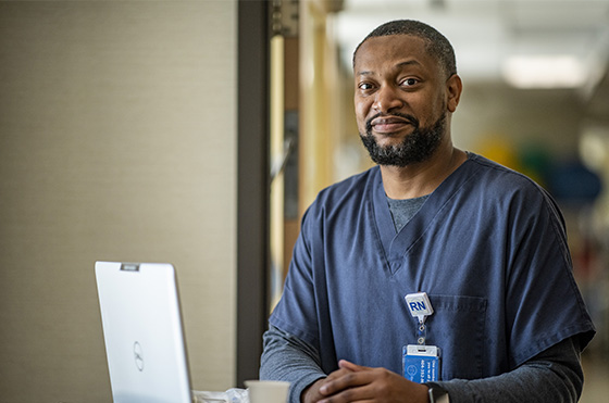 A nurse wearing dark blue scrubs and a name badge with 