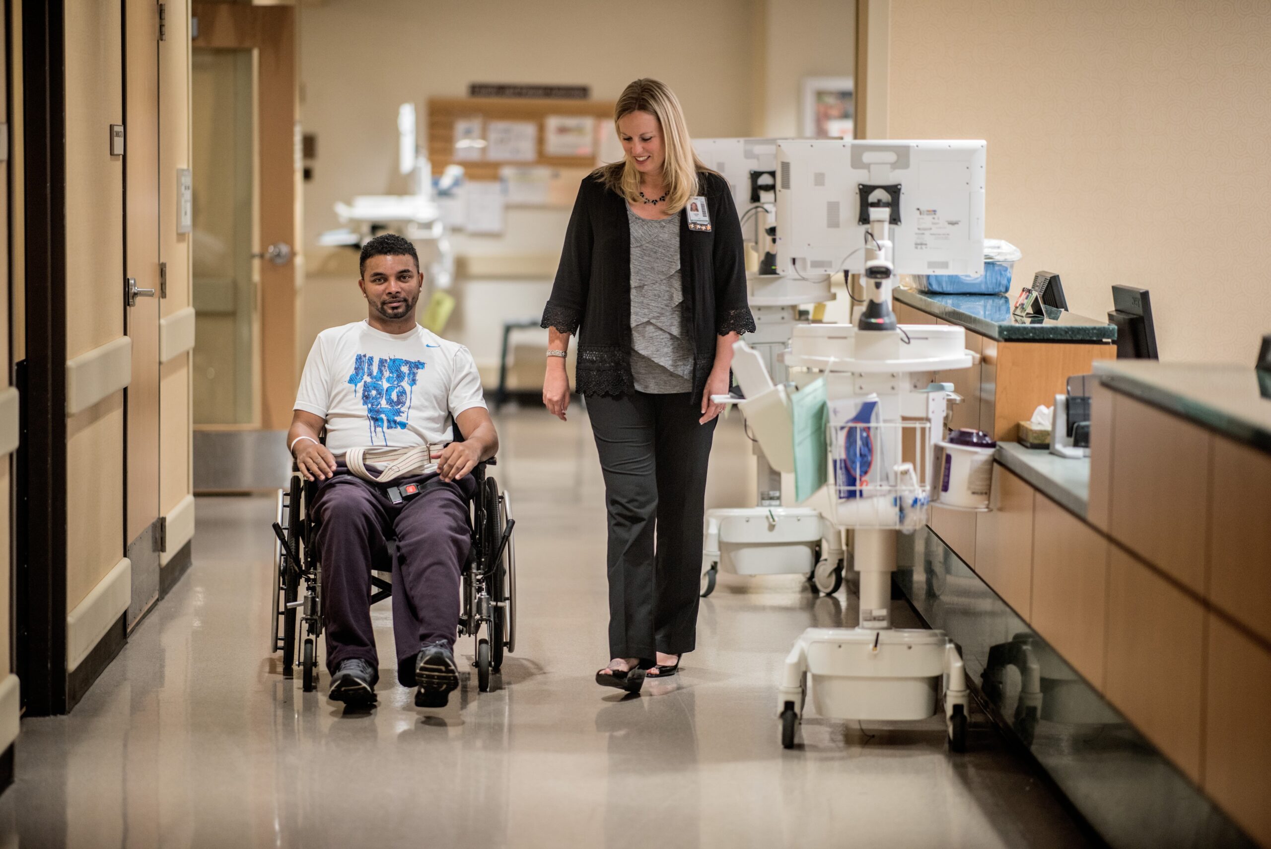 Psychologist walking down Shepherd Center hallways alongside a male patient in a wheelchair.