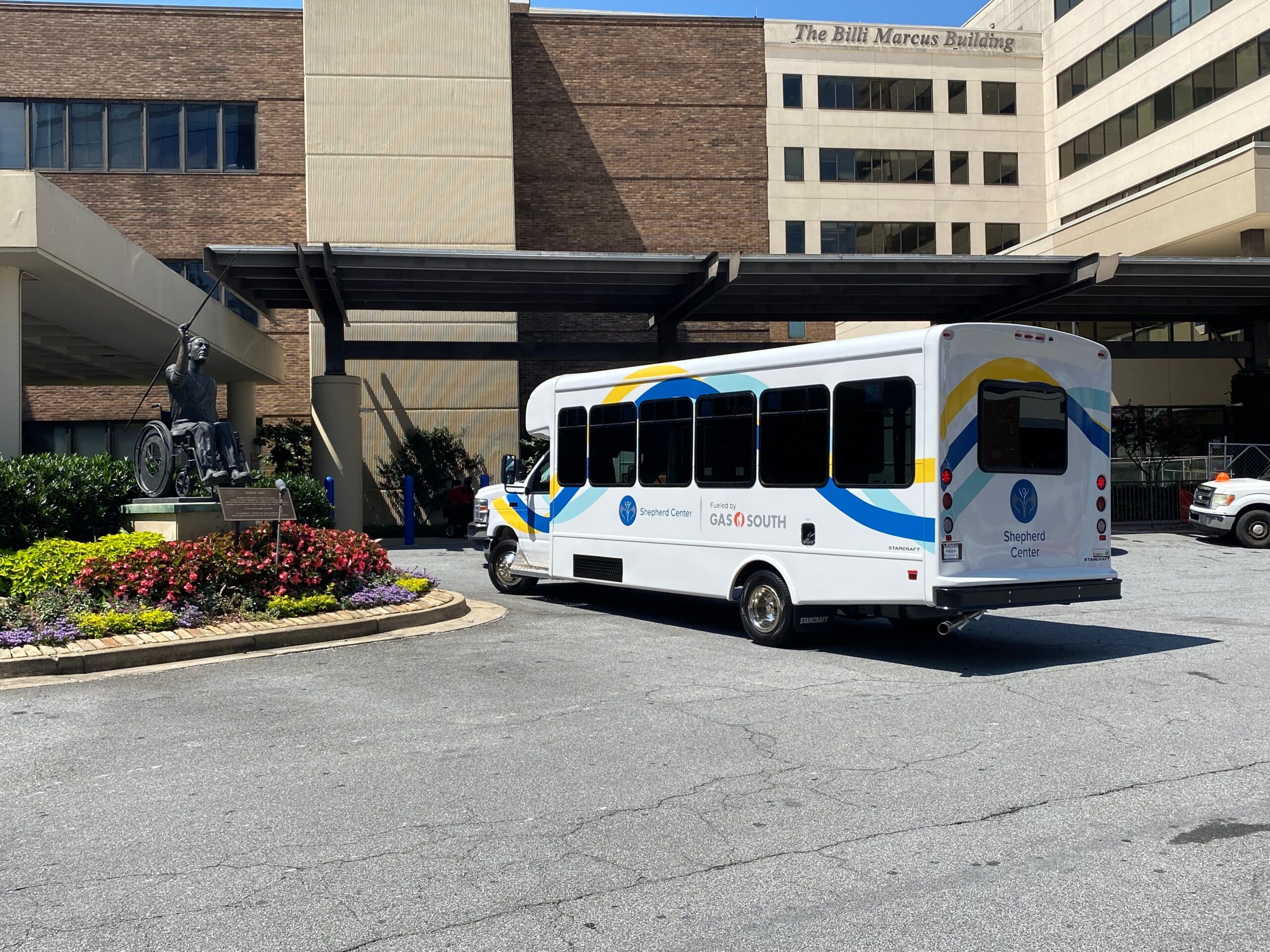 A white shuttle bus with colorful stripes is parked in front of a building labeled 