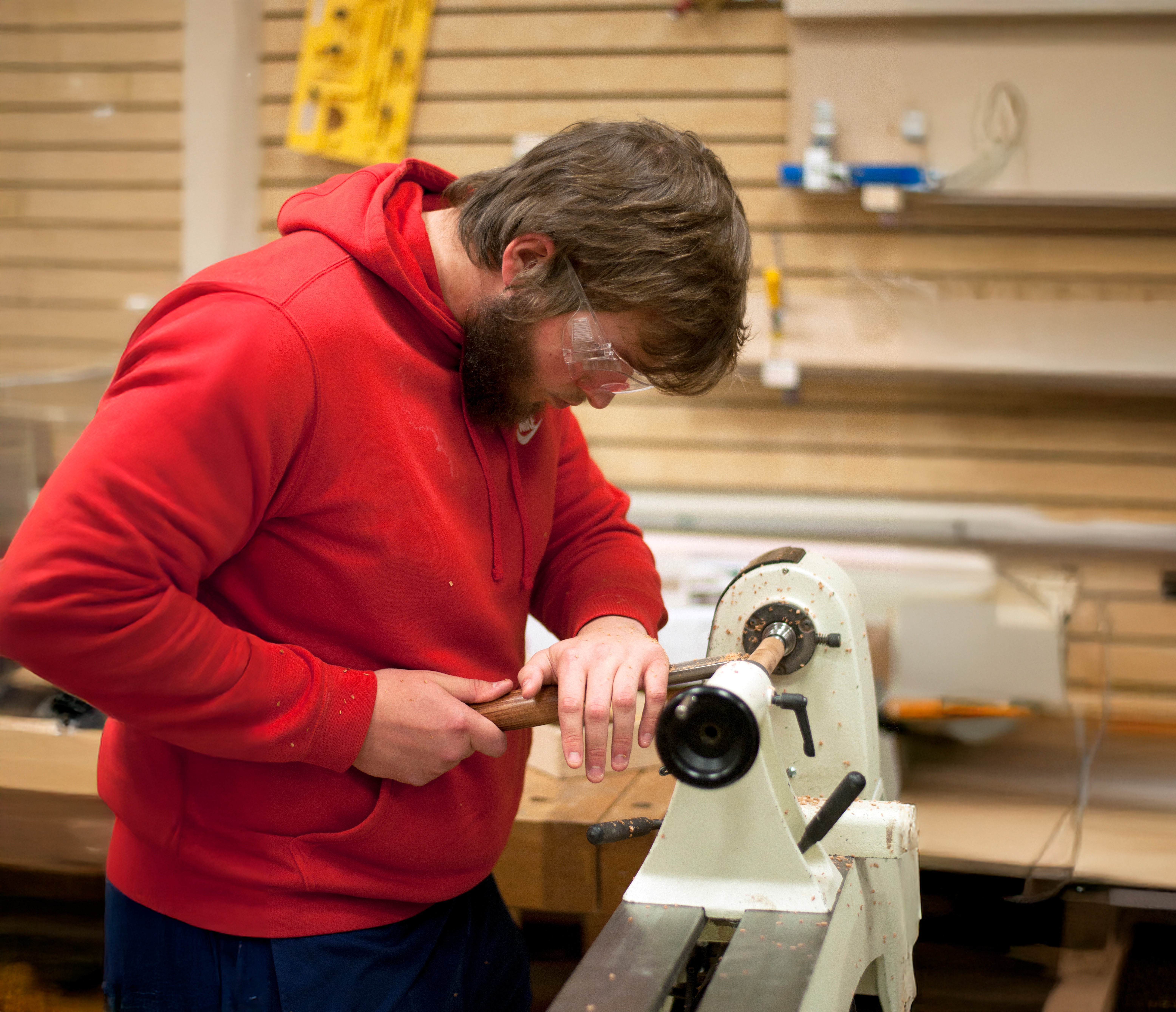 Male using an electric sander on a wood dowel while wearing safety glasses.