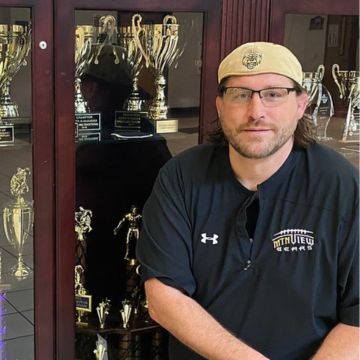 A person wearing a beige cap and dark sports shirt with 