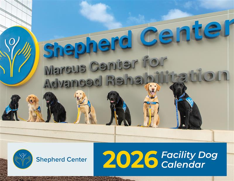 Seven facility dogs wearing blue vests sit in a row in front of the Shepherd Center’s Marcus Center for Advanced Rehabilitation sign. Text reads 