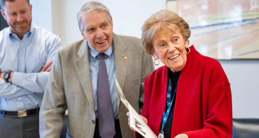 Dr. Apple smiles as he looks at an old edition of Shepherd's Spinal Column magazine that Alana Shepherd is holding.