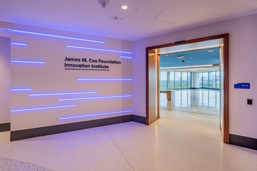 Entrance to the James M. Cox Foundation Innovation Institute. The wall features illuminated blue lines, and a doorway leads to a bright, open room.