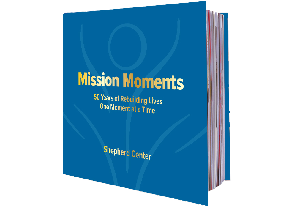 Blue hardcover book titled “Mission Moments: 50 Years of Rebuilding Lives One Moment at a Time” by Shepherd Center, featuring simple line art and gold lettering on the cover.