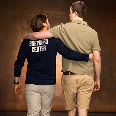 Two people stand side by side with their arms around each other. One wears a navy jacket with 