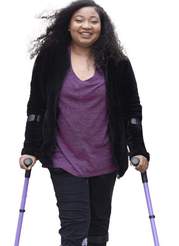 A smiling woman with long curly hair uses purple forearm crutches. She is wearing a purple top, black jacket, and black pants, walking confidently against a plain white background.